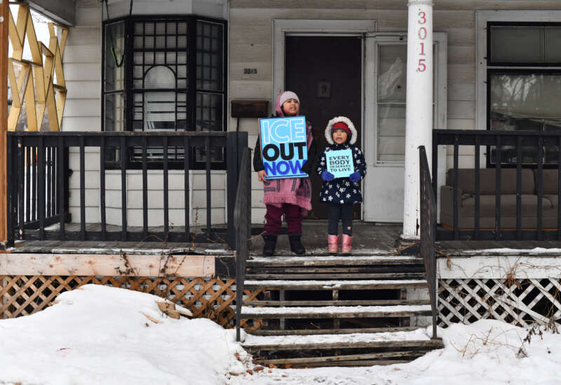 Children hold signs on the stoop of a house as protesters march against Immigration and Customs Enforcement (ICE) and the fatal shooting of Renee Good by an ICE agent in Minneapolis, Minnesota, on January 10, 2026.