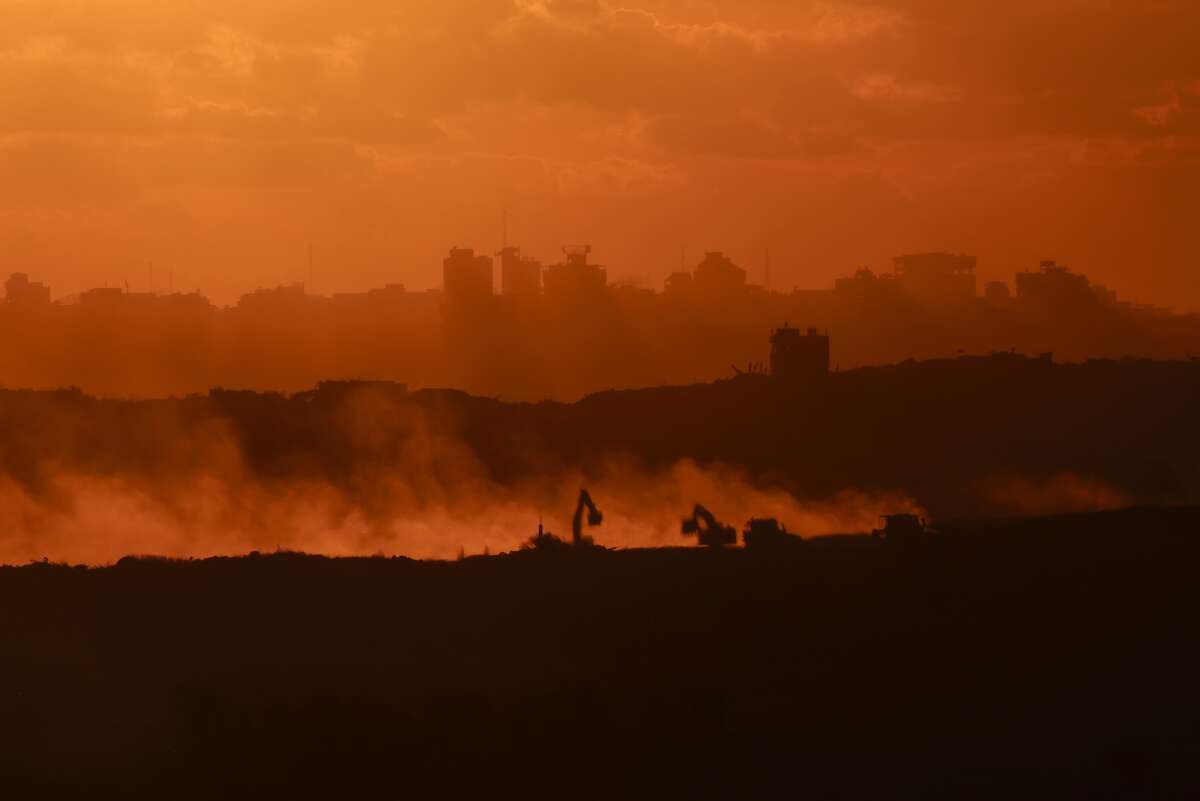 This picture taken from a position on the Israeli border with the Gaza Strip, shows the sun setting behind destroyed buildings as Israeli bulldozers work amid a ceasefire between Israel and Palestinian factions in the besieged territory on October 14, 2025.