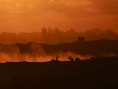 This picture taken from a position on the Israeli border with the Gaza Strip, shows the sun setting behind destroyed buildings as Israeli bulldozers work amid a ceasefire between Israel and Palestinian factions in the besieged territory on October 14, 2025.