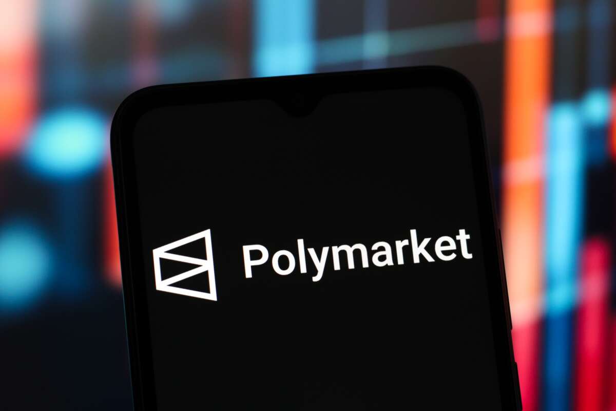 The Polymarket logo is seen displayed on a smartphone screen.