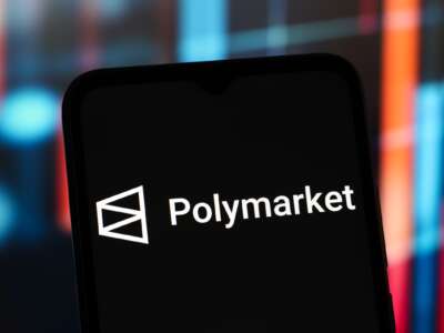 The Polymarket logo is seen displayed on a smartphone screen.