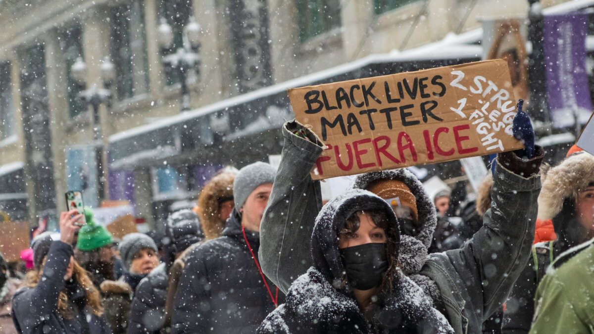A protester holds a sign reading "Black Lives Matter Fuera ICE. 2 Struggles 1 Fight."