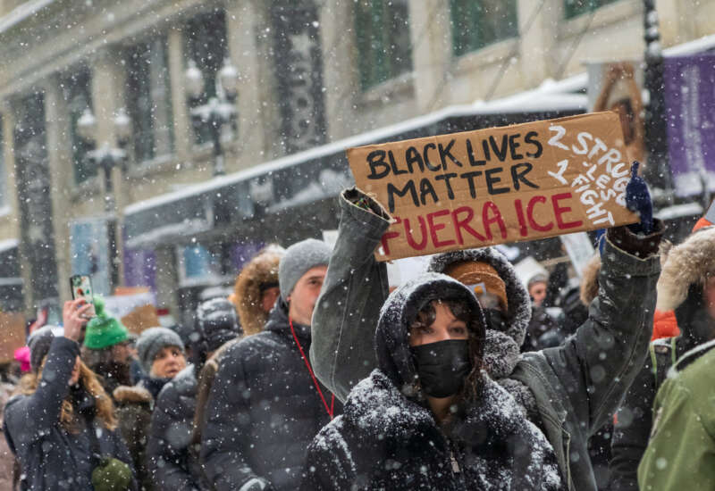A protester holds a sign reading "Black Lives Matter Fuera ICE. 2 Struggles 1 Fight."