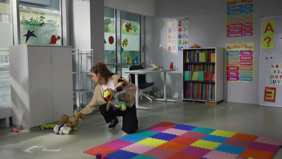 Teacher collects toys from floor at nursery school