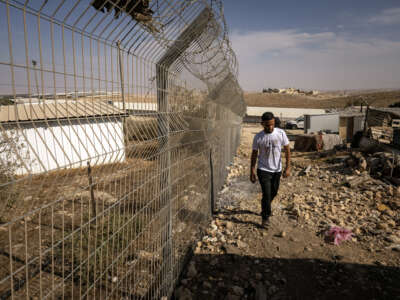 A Palestinian man walks along the fence that separates the village of Umm al-Khair from an Israeli settlement in the occupied West Bank, on November 2, 2025.