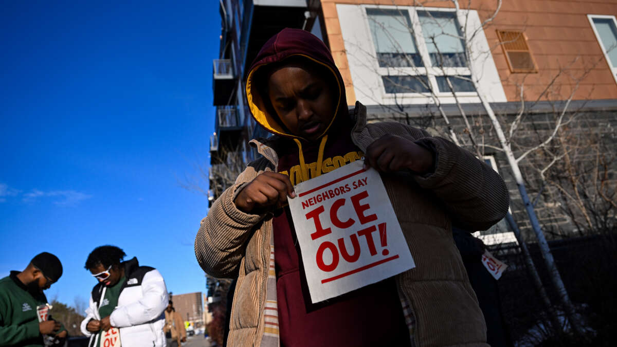 ICE watcher Fahad adjust an applies a piece of fabric to his sweater that reads "Neighbors Say ICE Out!" as he patrols the community around the Riverside Plaza complex in the Cedar-Riverside neighborhood on January 9, 2026, in Minneapolis, Minnesota. The volunteers are patrolling their community, which is predominantly Somali, as they watch for federal agents who are in the city conducting an immigration operation.