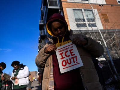 ICE watcher Fahad adjust an applies a piece of fabric to his sweater that reads "Neighbors Say ICE Out!" as he patrols the community around the Riverside Plaza complex in the Cedar-Riverside neighborhood on January 9, 2026, in Minneapolis, Minnesota. The volunteers are patrolling their community, which is predominantly Somali, as they watch for federal agents who are in the city conducting an immigration operation.