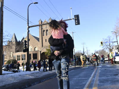 A person carries a child away from the scene where ICE agents were confronted by protestors after they arrested people from a residence on January 13, 2026, in Minneapolis, Minnesota.