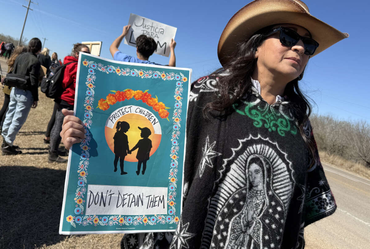 A protester holds a sign reading "Protect Children / Don't Detain Them" as people gather during a demonstration and vigil outside the South Texas Family Residential Center in Dilley, Texas, on January 28, 2026.