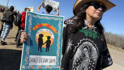 A protester holds a sign reading "Protect Children / Don't Detain Them" as people gather during a demonstration and vigil outside the South Texas Family Residential Center in Dilley, Texas, on January 28, 2026.
