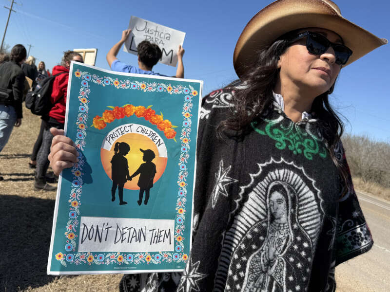 A protester holds a sign reading "Protect Children / Don't Detain Them" as people gather during a demonstration and vigil outside the South Texas Family Residential Center in Dilley, Texas, on January 28, 2026.