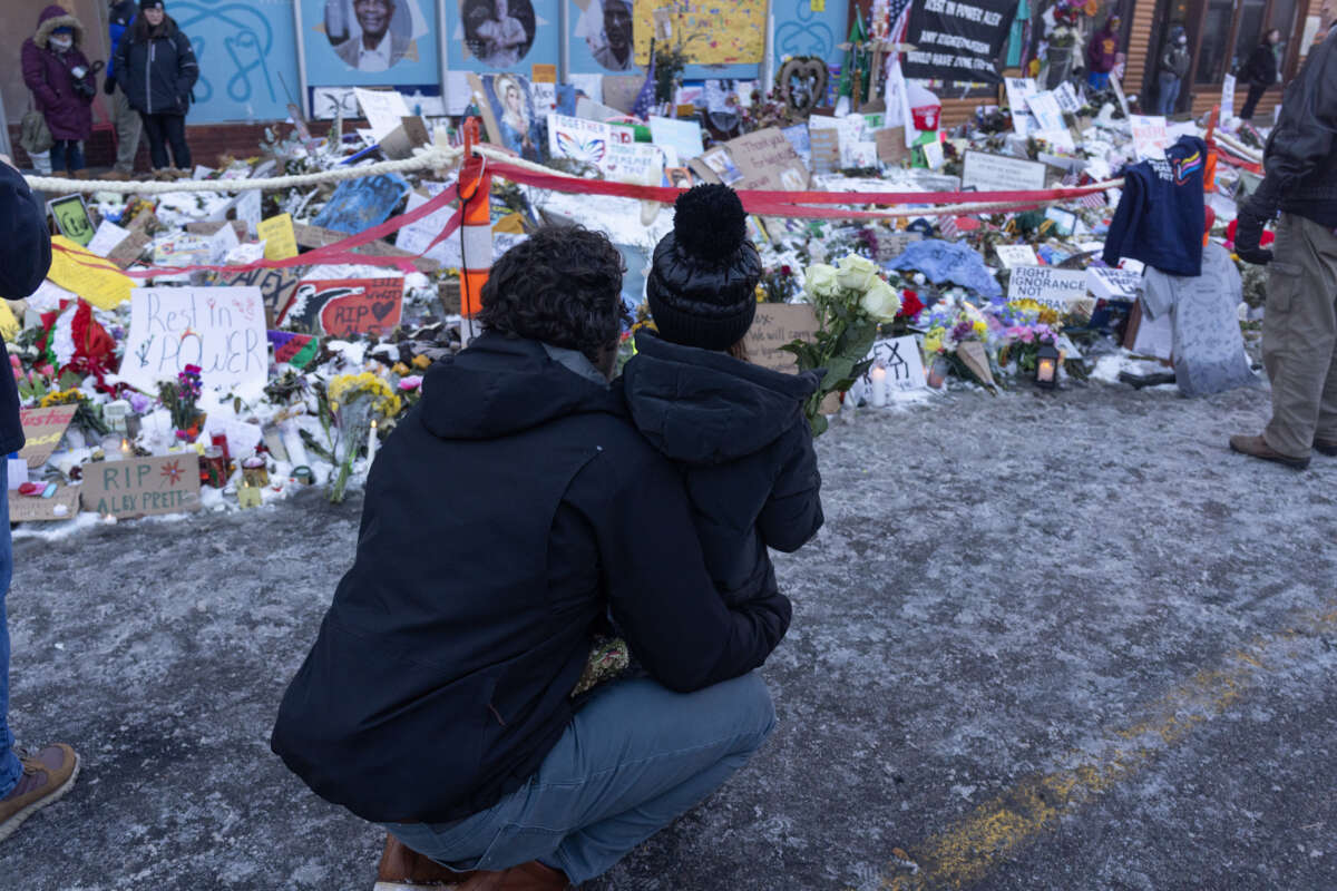 Two people look at a street memorial marking the spot where Alex Pretti was killed by ICE agents in Minneapolis