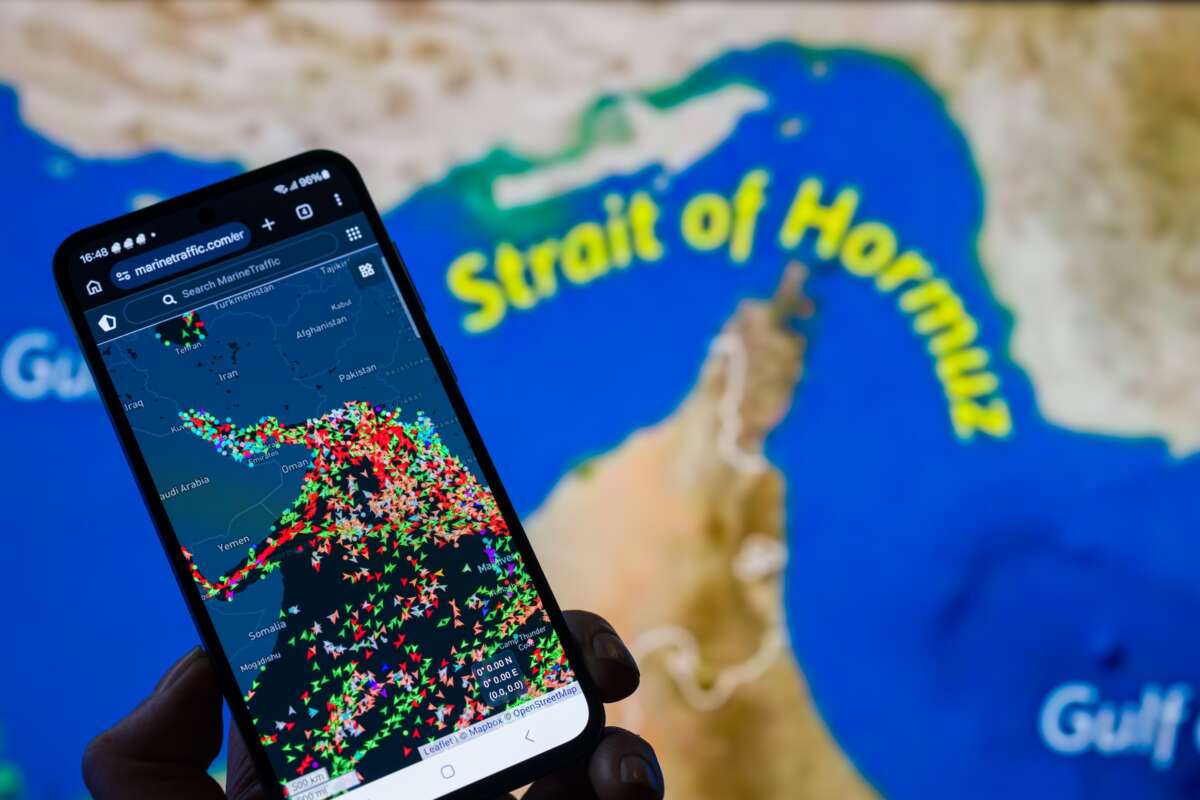 A MarineTraffic map showing ship movements in the Strait of Hormuz is displayed on a smartphone screen with a map in the background in this photo illustration, as commercial vessel traffic through the key oil shipping lane decreases amid the ongoing conflict involving Iran.