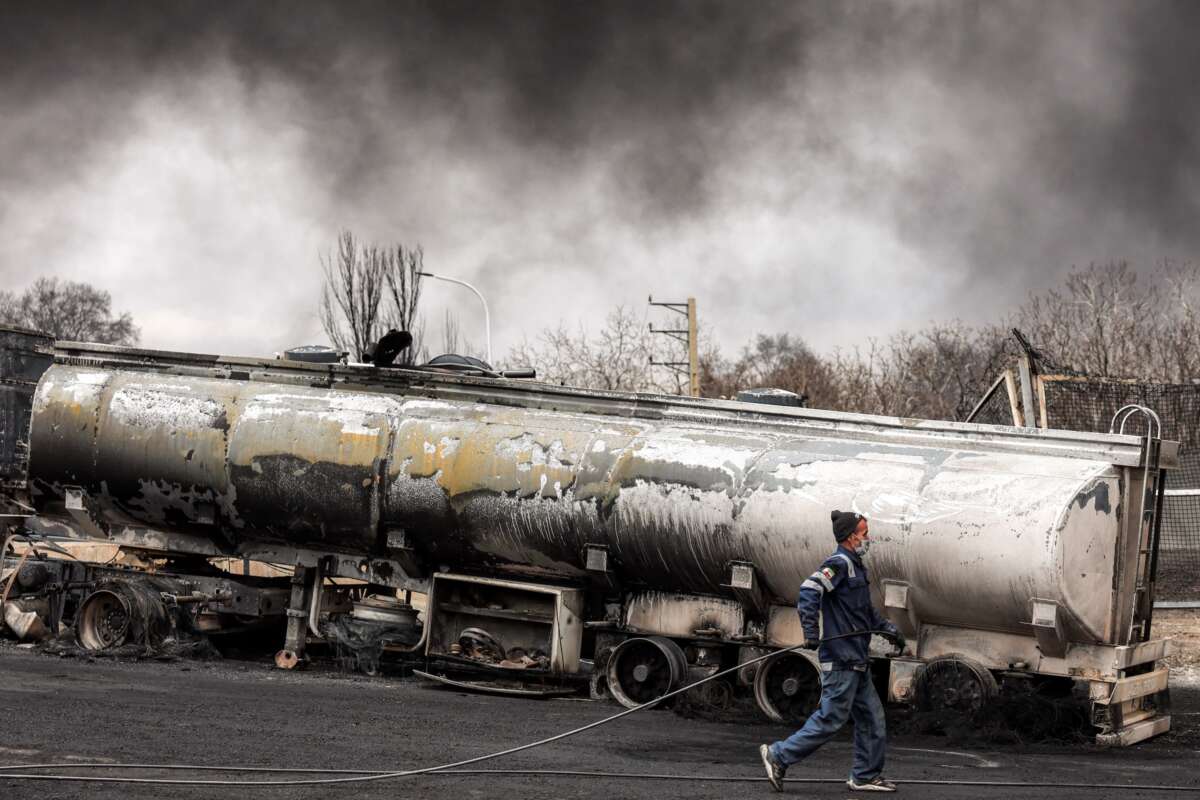 An Iranian civil defence member walks with a hose next to a destroyed fuel tanker vehicle near an ongoing fire following an overnight airstrike on the Shahran oil refinery in northwestern Tehran on March 8, 2026.