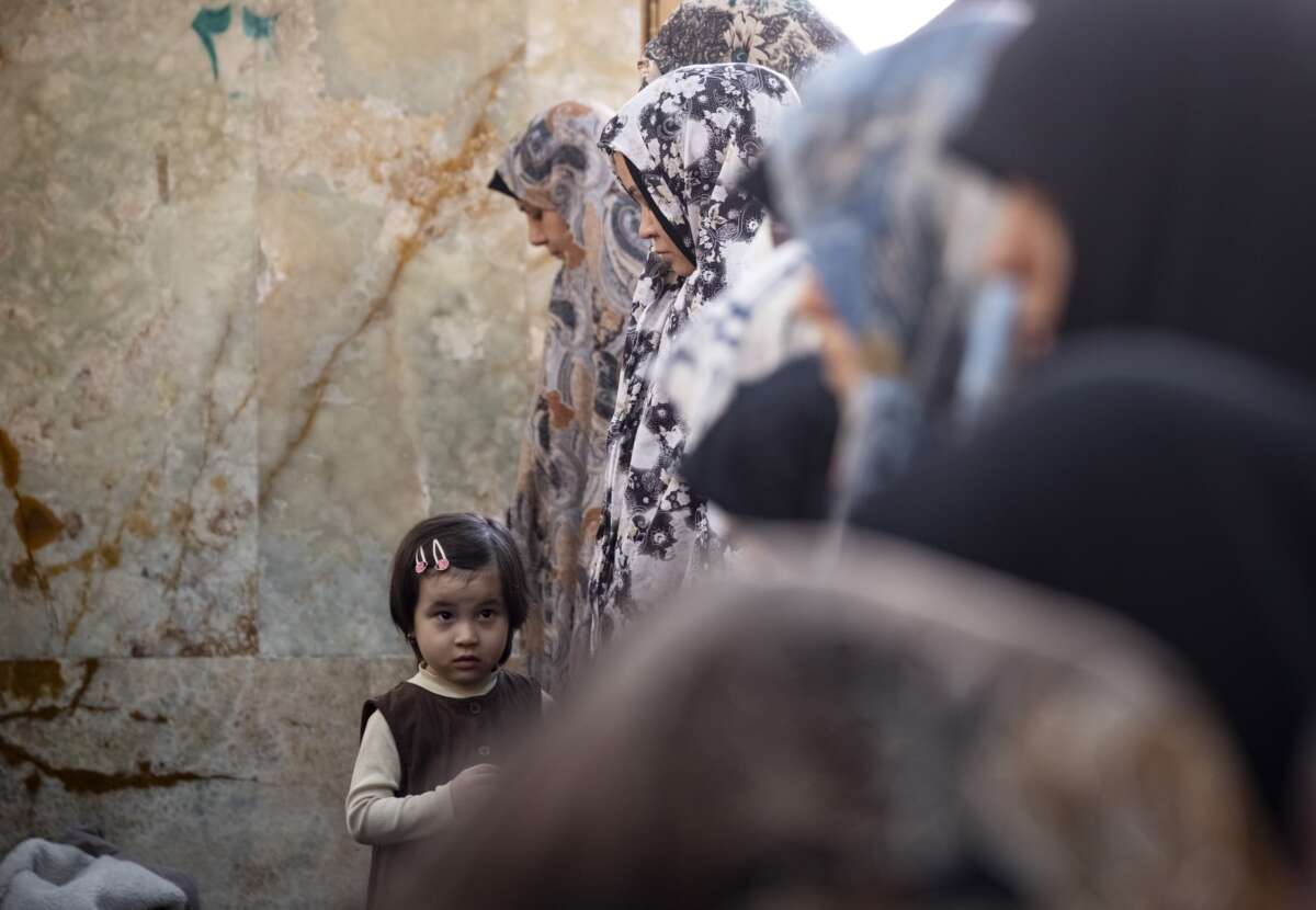 A young girl looks on as veiled worshippers pray during an Eid al-Fitr mass prayer ceremony in the Shahr-e Rey neighborhood in southern Tehran, Iran, on March 21, 2026, amid the United States and Israel's bombardments in Iran.