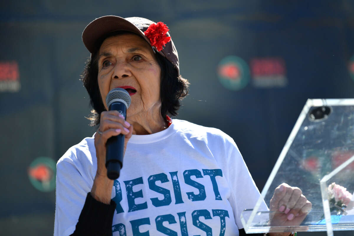 Dolores Huerta holding a microphone and wearing a shirt that reads "resist"