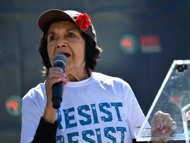 Dolores Huerta holding a microphone and wearing a shirt that reads "resist"