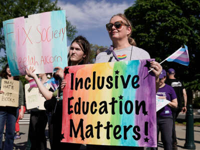A woman is holding a sing that has the rainbow painted on it with words that read "Inclusive Education Matters!"