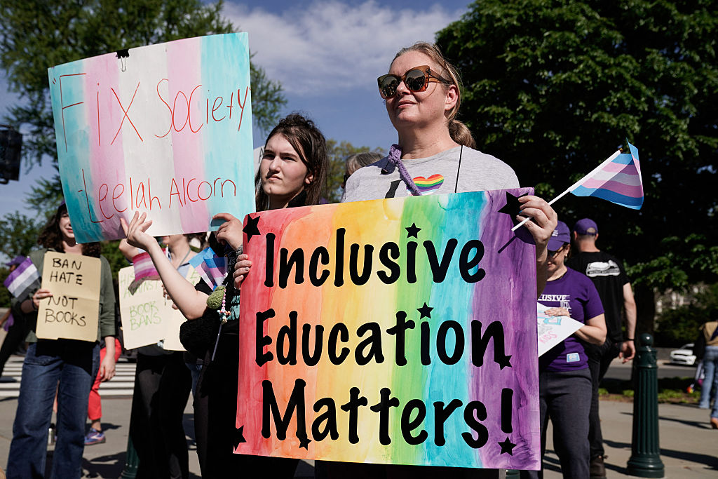 A woman is holding a sing that has the rainbow painted on it with words that read "Inclusive Education Matters!"