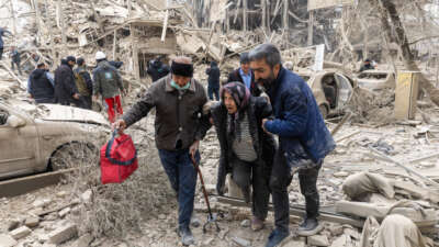 An elderly woman is helped from the scene of a strike on a residential building on March 16, 2026, in Tehran, Iran.