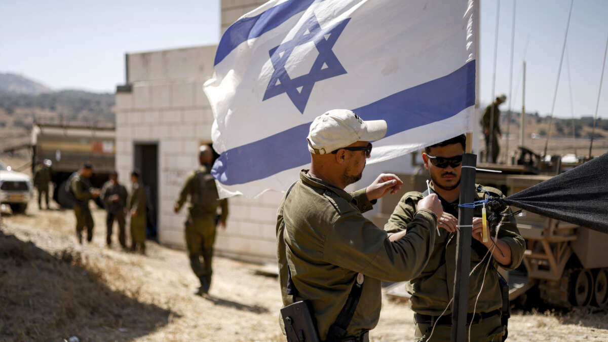 Israeli army soldiers add zip ties to the mast of an Israeli flag flying at a special area for exercises during a military drill in the Israeli-annexed Golan Heights on July 8, 2025.