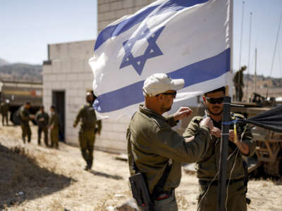 Israeli army soldiers add zip ties to the mast of an Israeli flag flying at a special area for exercises during a military drill in the Israeli-annexed Golan Heights on July 8, 2025.