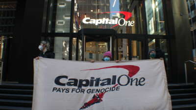 On April 21, 2026, three demonstrators held a banner outside of Capital One’s Midtown Manhattan offices, protesting the bank’s loan to Elbit Systems, set to expire on April 24, 2026.
