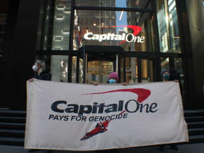 On April 21, 2026, three demonstrators held a banner outside of Capital One’s Midtown Manhattan offices, protesting the bank’s loan to Elbit Systems, set to expire on April 24, 2026.
