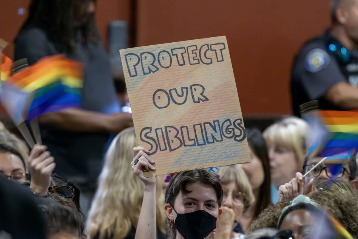 A person holds a sign in opposition to a policy that would require school staff to "out" students to their parents if they ask to be identified by a gender not listed on their birth certificate on July 20, 2023 in Chino, California.