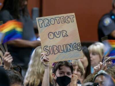 A person holds a sign in opposition to a policy that would require school staff to "out" students to their parents if they ask to be identified by a gender not listed on their birth certificate on July 20, 2023 in Chino, California.
