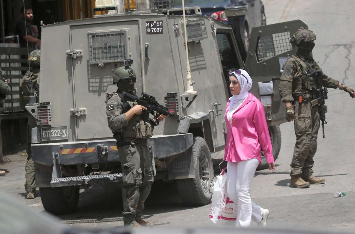 A Palestinian girl walks past Israeli soldiers conducting a military operation in the central market of Nablus on May 3, 2026.