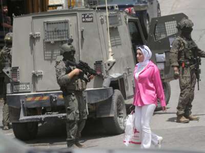 A Palestinian girl walks past Israeli soldiers conducting a military operation in the central market of Nablus on May 3, 2026.