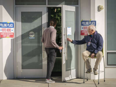 An election worker holds the door open for people casting their votes at the Washington-Liberty Annex polling location in Arlington, Virginia, on April 21, 2026.