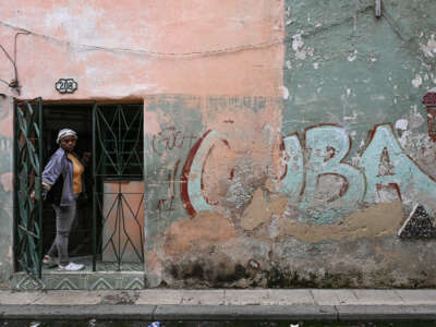 A woman peeks out from the doorway of her home next to a wall with a graffiti reading "CUBA" on a street in Havana, Cuba, on May 6, 2026.