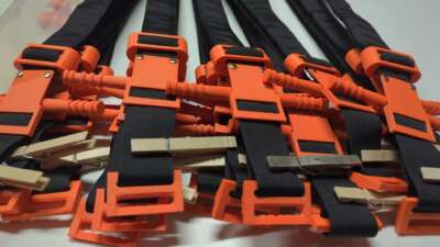 3D-printed tourniquets manufactured by the Distributed Medical Device Manufacturing collective (DMDM) are stacked on a table after a work party held in April 2026.