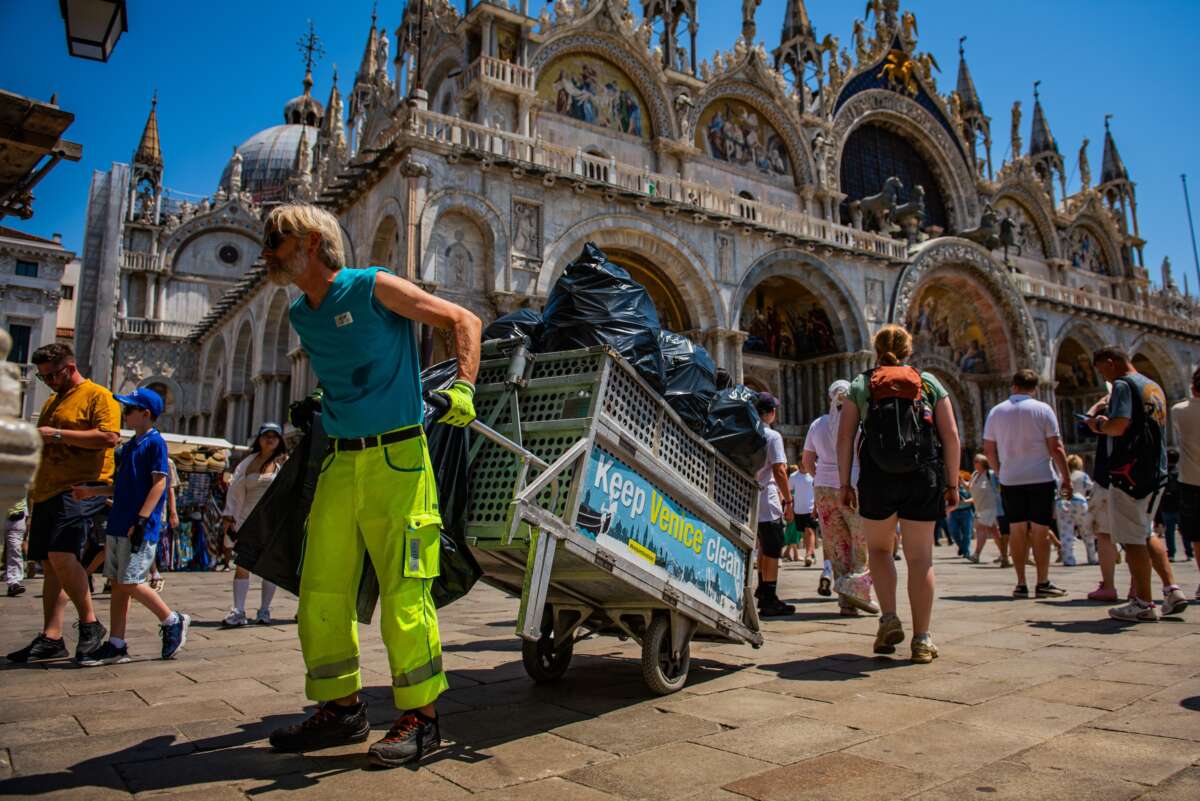 A waste-collection worker hauls trash bags through crowds in St Mark's Square, at the height of a severe heatwave, on June 24, 2026 in Venice, Italy.