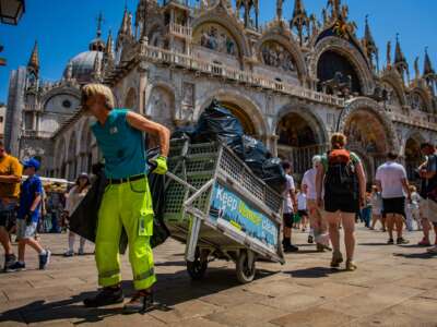 A waste-collection worker hauls trash bags through crowds in St Mark's Square, at the height of a severe heatwave, on June 24, 2026 in Venice, Italy.