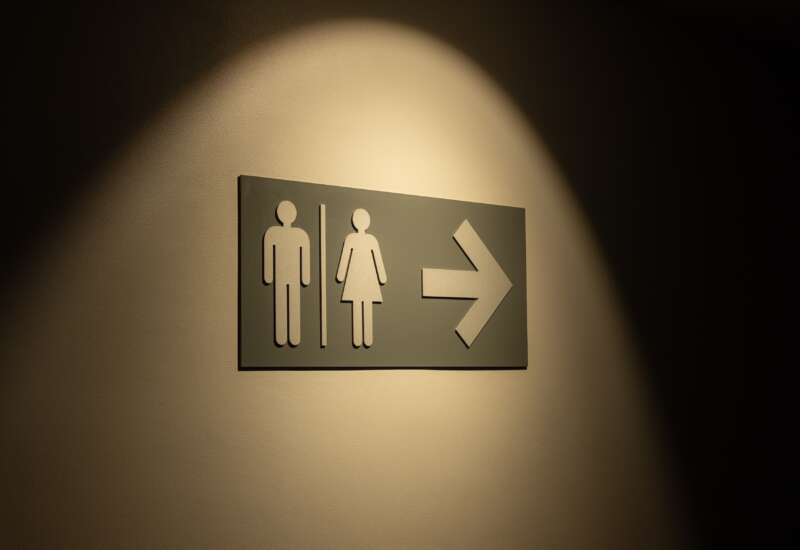 Illuminated directional sign with male and female restroom symbols and an arrow