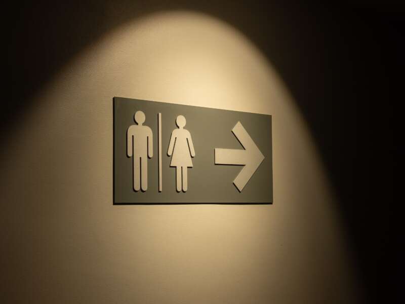 Illuminated directional sign with male and female restroom symbols and an arrow