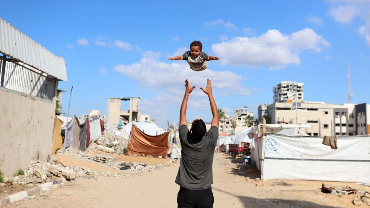 A displaced Palestinian man plays with his son in a displacement camp in Gaza City, Palestine, on November 26, 2025.
