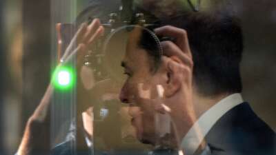 Elon Musk is seen through glass at the Ronald V. Dellums Federal Building and U.S. Courthouse in Oakland, California, passing through security as he continues his testimony in the OpenAI trial on April 29, 2026.
