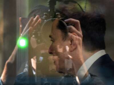 Elon Musk is seen through glass at the Ronald V. Dellums Federal Building and U.S. Courthouse in Oakland, California, passing through security as he continues his testimony in the OpenAI trial on April 29, 2026.