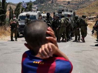 A Palestinian boy looks on as Israeli forces stand guard before Palestinians gathering to protest threats of confiscation of their land in the Palestinian village of Idna, west of Hebron in the occupied West Bank, on June 12, 2026.