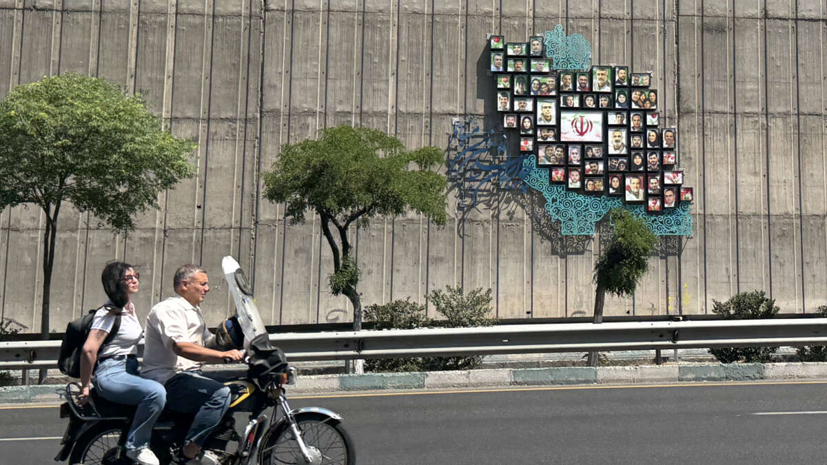 A man and woman ride their motor bike past a map of Iran with the images of some of those killed in the Israeli-U.S. war against the nation, erected on a wall along the highway in Tehran, Iran, on June 17, 2026.
