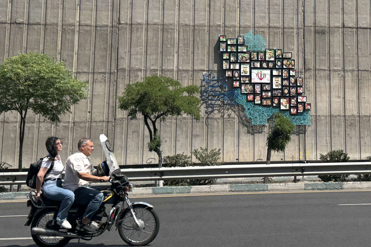 A man and woman ride their motor bike past a map of Iran with the images of some of those killed in the Israeli-U.S. war against the nation, erected on a wall along the highway in Tehran, Iran, on June 17, 2026.