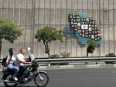 A man and woman ride their motor bike past a map of Iran with the images of some of those killed in the Israeli-U.S. war against the nation, erected on a wall along the highway in Tehran, Iran, on June 17, 2026.