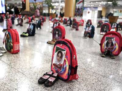Portraits of schoolchildren killed in an air strike in Minab in February 2026 are pasted onto backpacks displayed alongside shoes at Hashemi Nejad International Airport in Mashhad on July 8, 2026, ahead of the final stage of the funeral of slain leader Ali Khamenei.