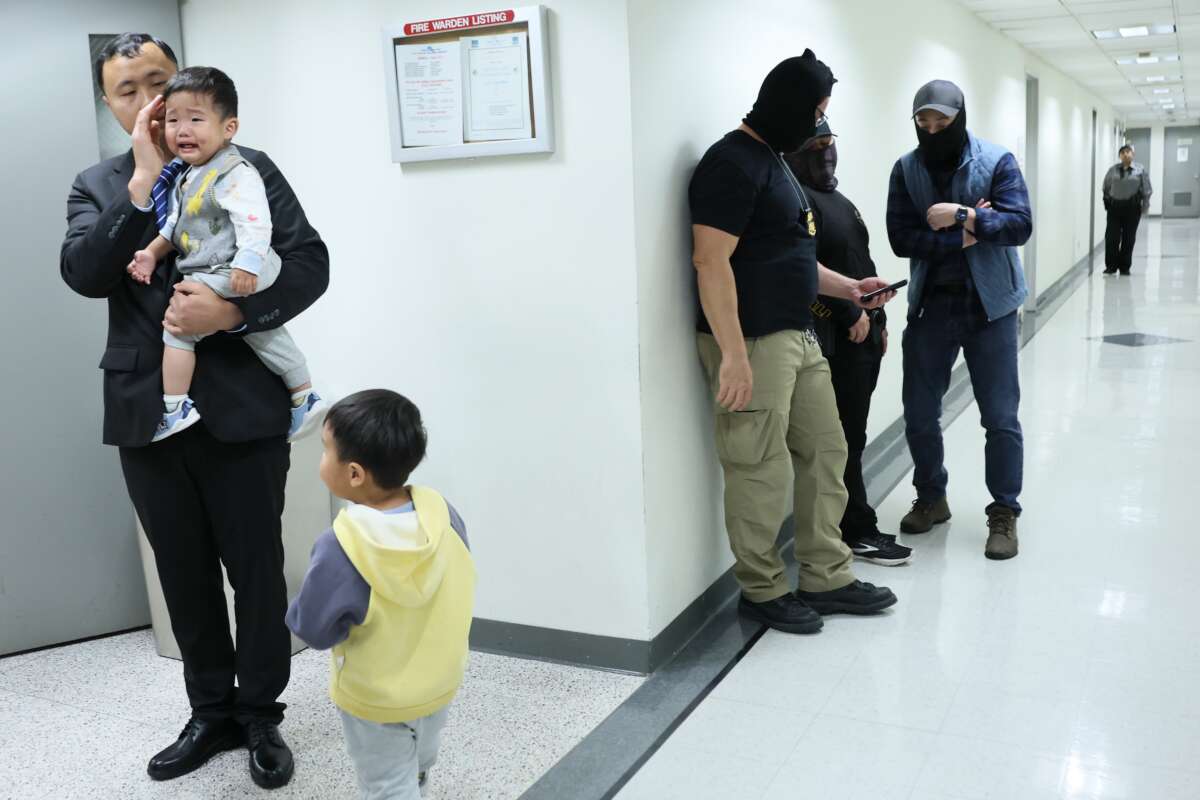 A man waits with children in the halls of immigration court as federal agents stand by, at the Jacob K. Javits Federal Building, on October 22, 2025, in New York City.