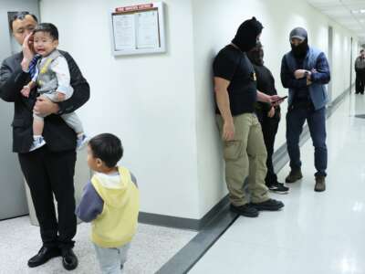 A man waits with children in the halls of immigration court as federal agents stand by, at the Jacob K. Javits Federal Building, on October 22, 2025, in New York City.