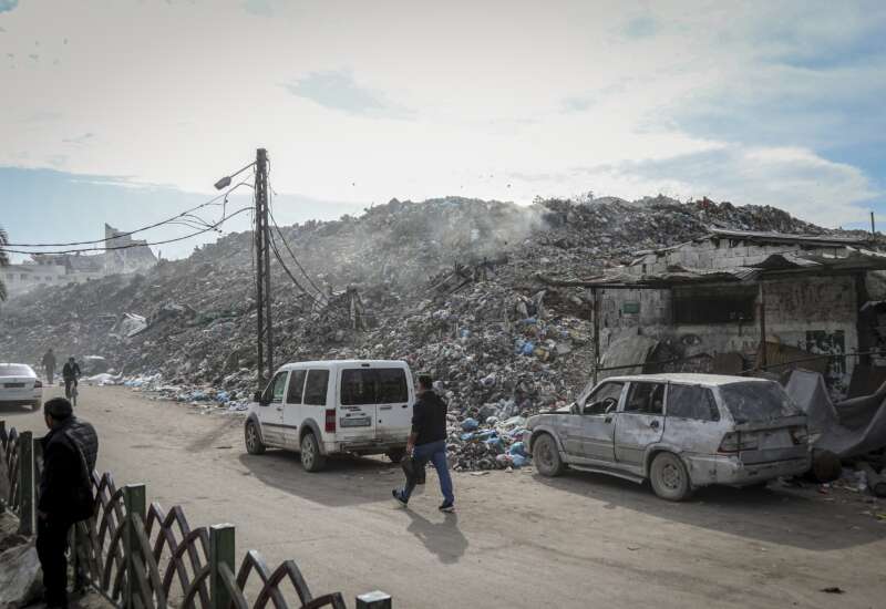 People walk and drive along a road beside large piles of debris at the destroyed Firas Market in Gaza City, on December 9, 2025. The public market, one of Gaza City's oldest and busiest commercial hubs, has been left buried under rubble and waste after widespread destruction from Israeli strikes and the collapse of basic municipal services.